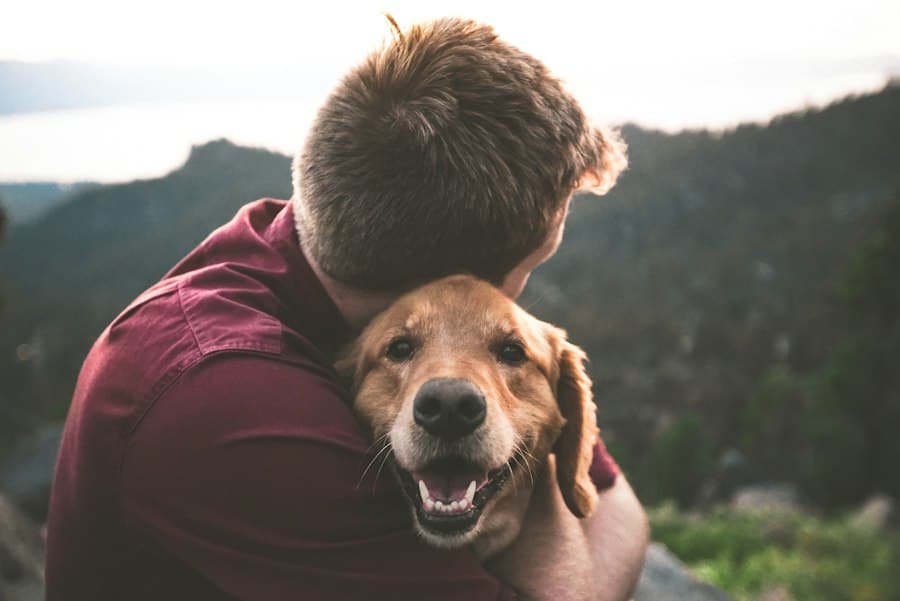 A man warmly hugging his smiling golden retriever outdoors